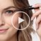 Model applying eyelash conditioner and play button in the middle